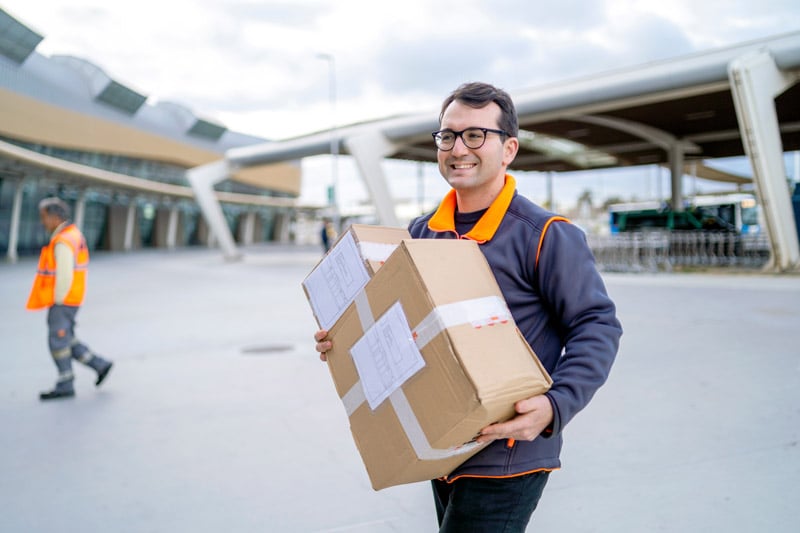 Delivery worker carrying a large package outside an airport terminal.