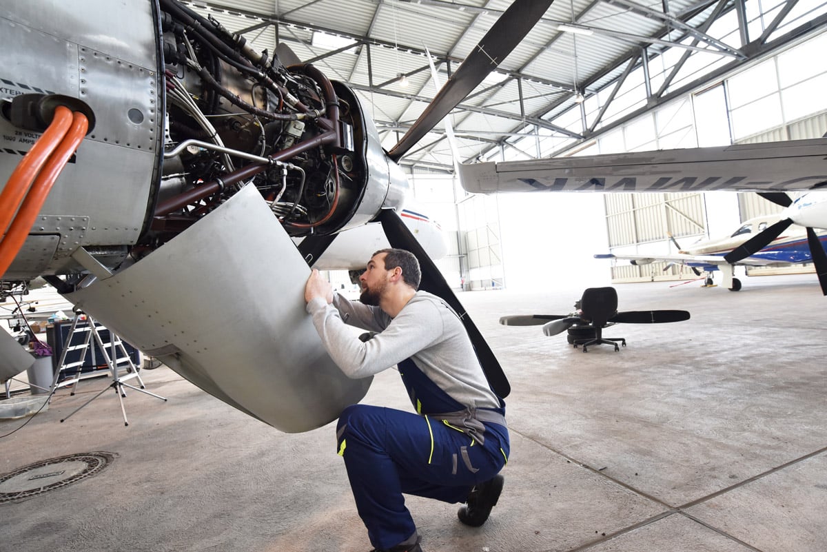 Aircraft technician inspecting and working on internal components of an airplane engine in a maintenance facility. 
