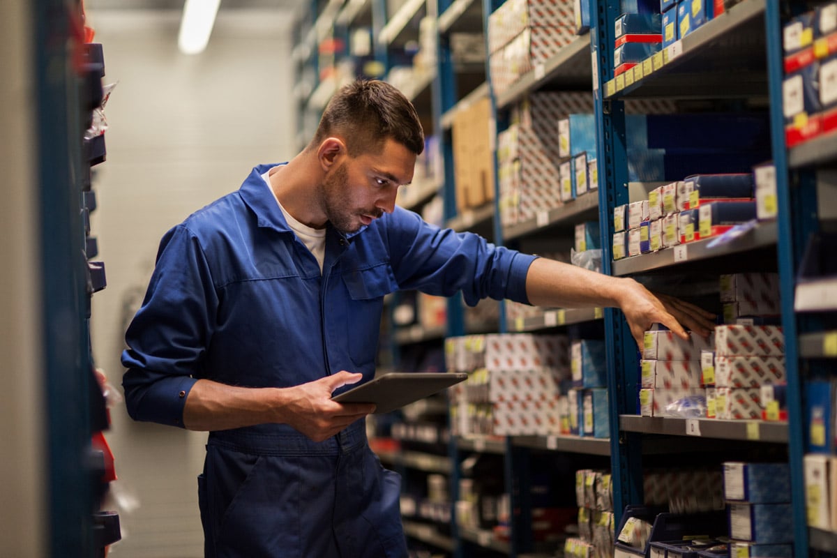 Warehouse worker using a tablet to check inventory while selecting items from storage shelves.