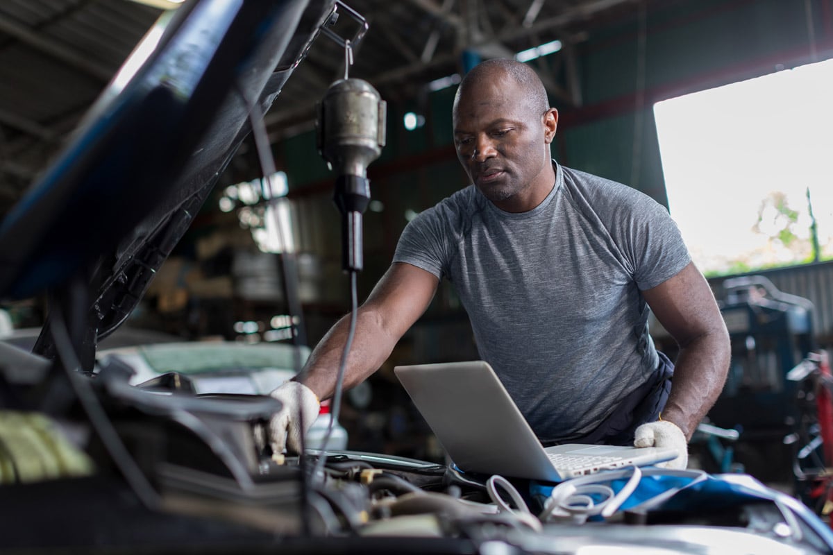 Mechanic using a laptop to diagnose a vehicle engine in a workshop. 
