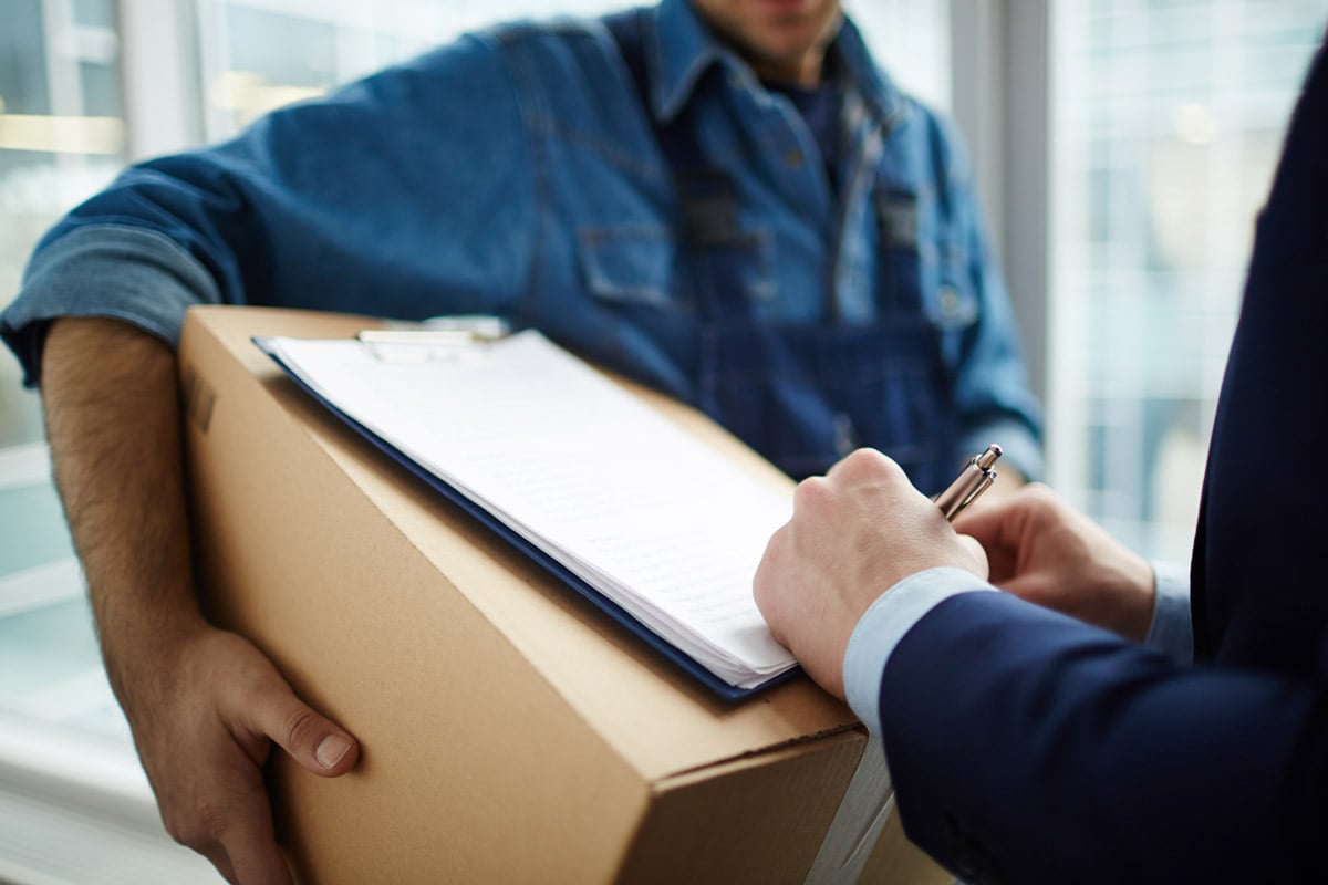 Person signing a delivery form on a clipboard while receiving a package from a courier. 
