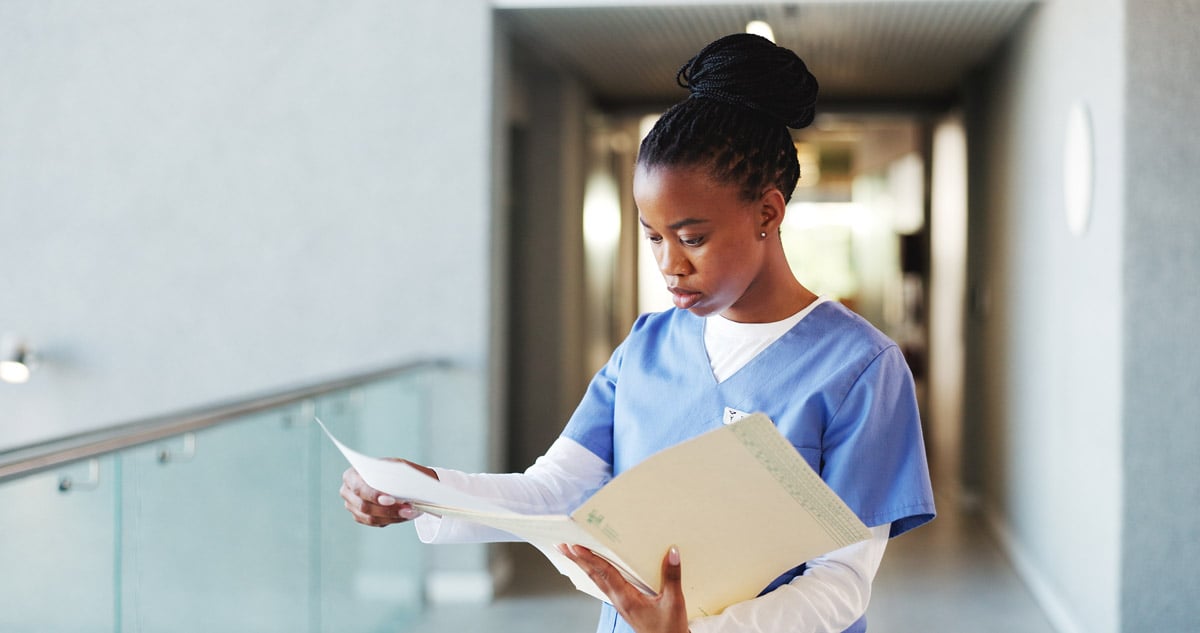 Healthcare professional in scrubs reviewing documents in a hospital hallway. 